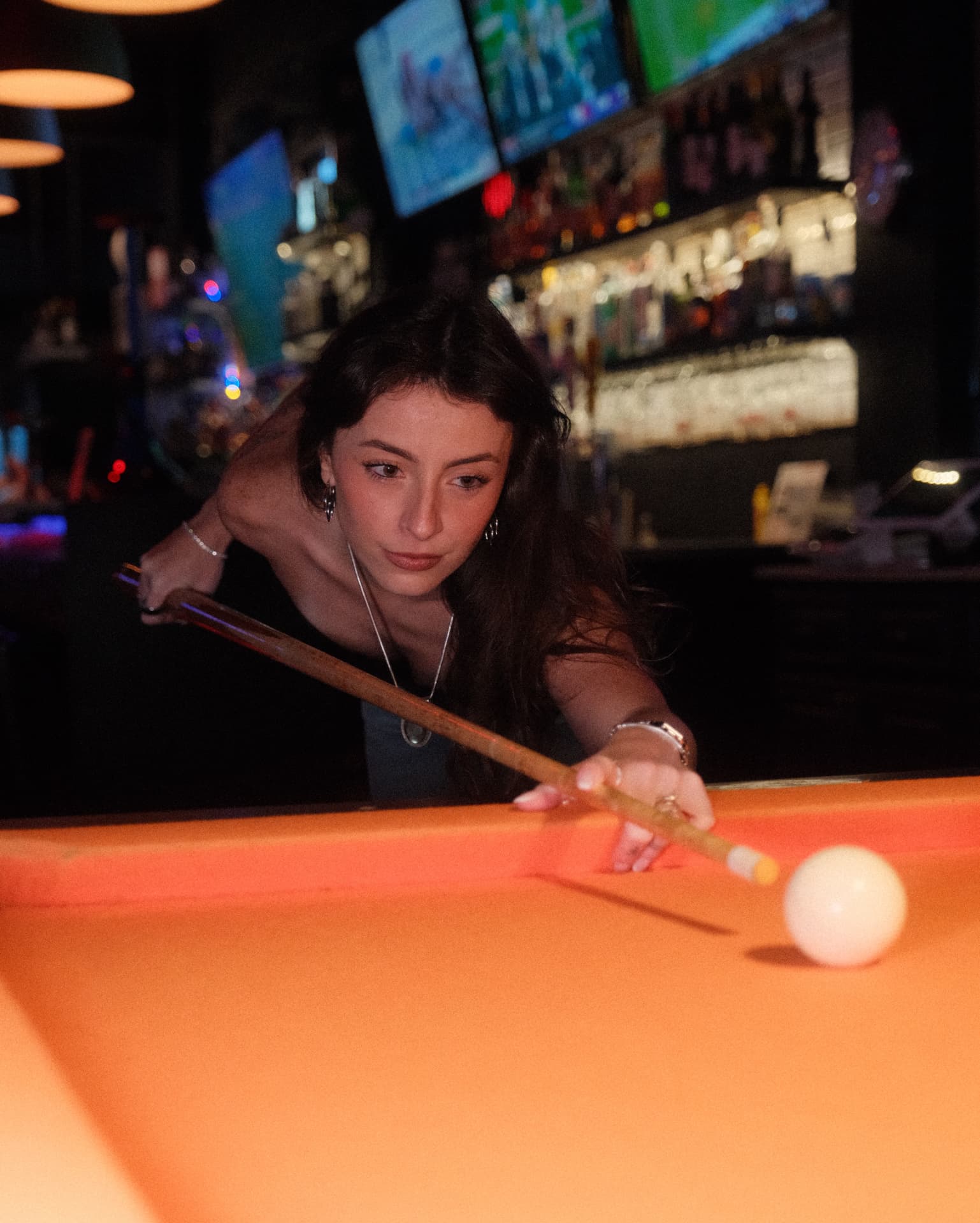 Lining up a shot at the bar, cue across the orange felt