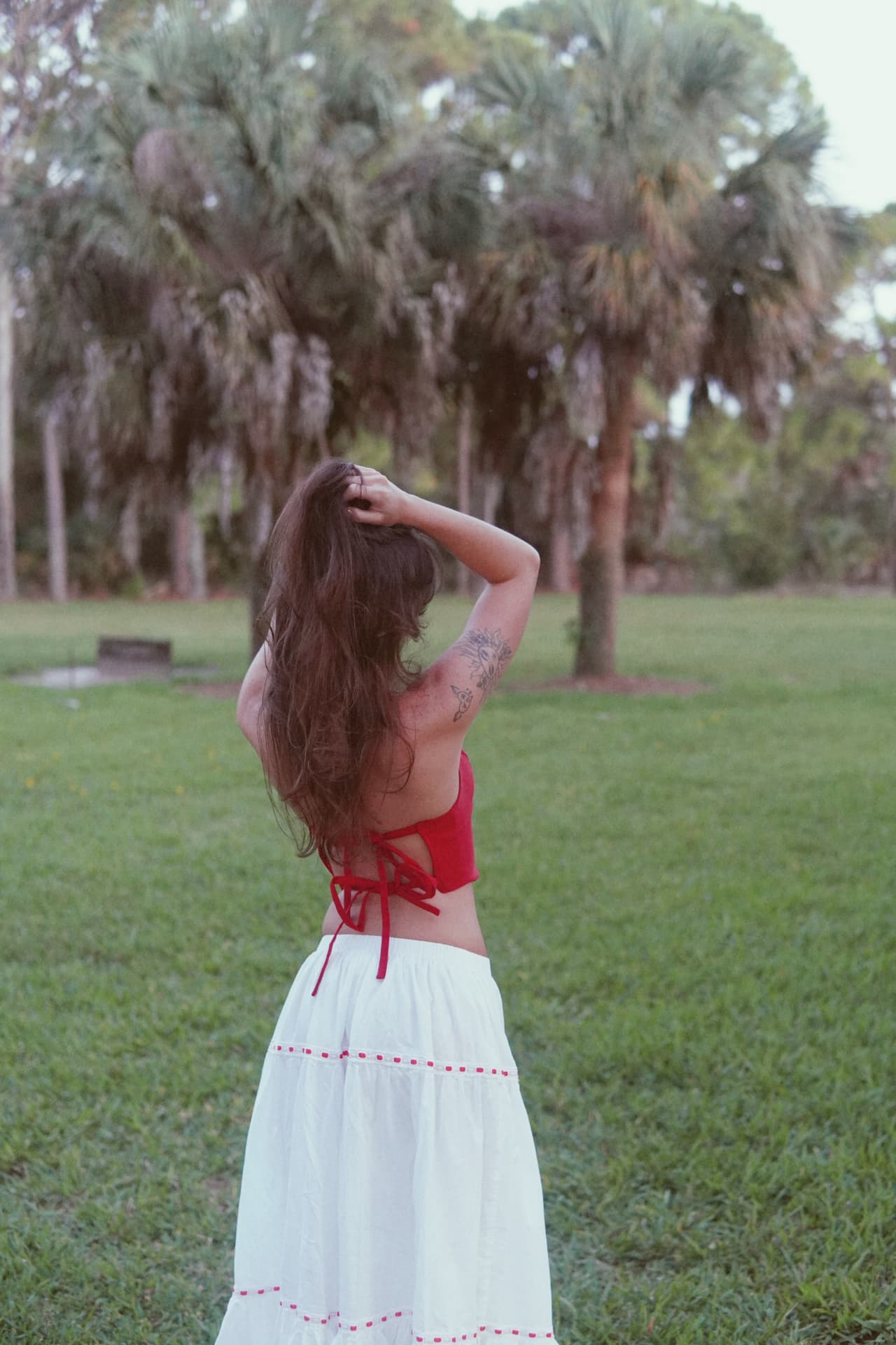 Back-facing portrait beneath palms, hand lifted through the hair