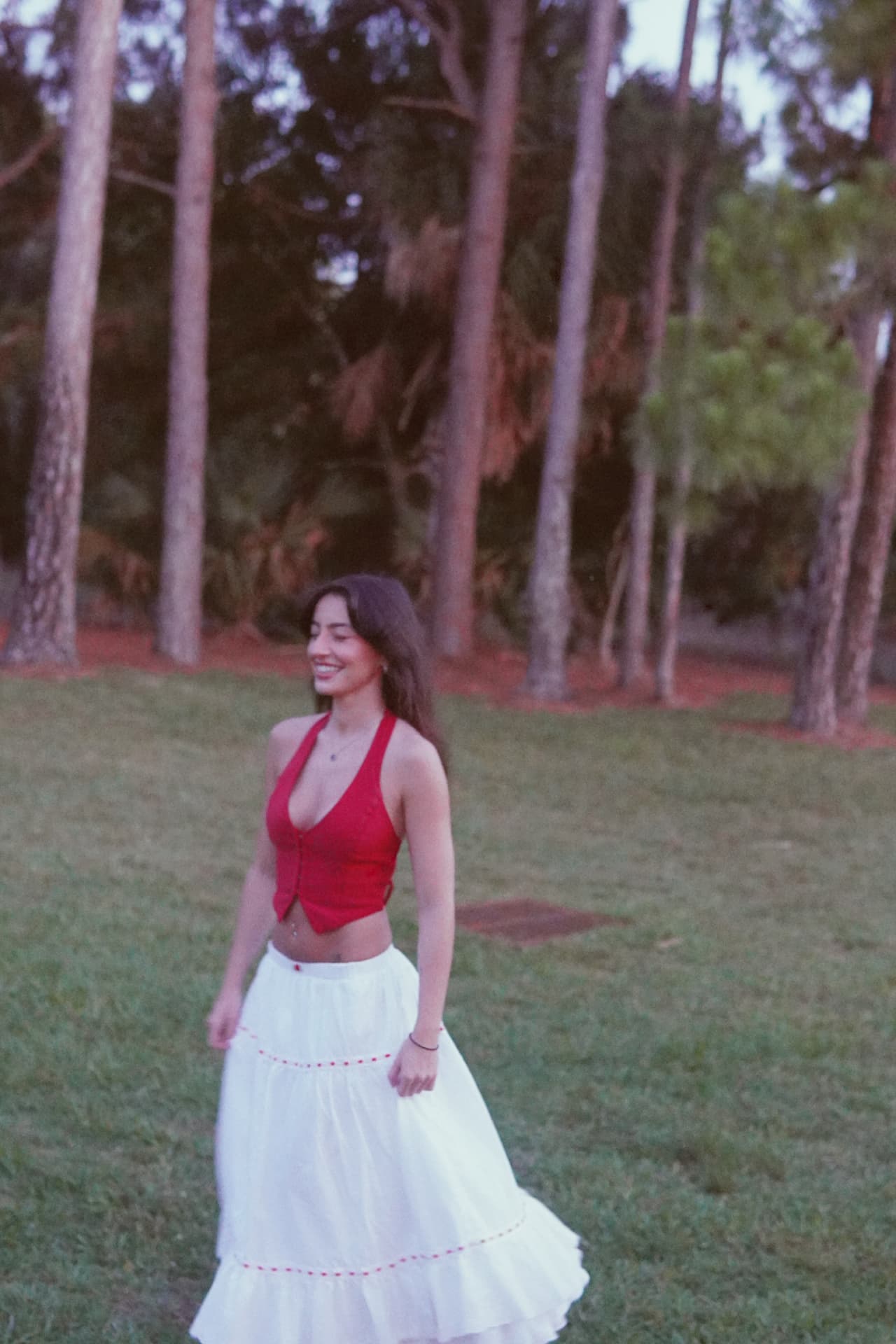Walking through the pines in a red halter top and long white skirt at dusk