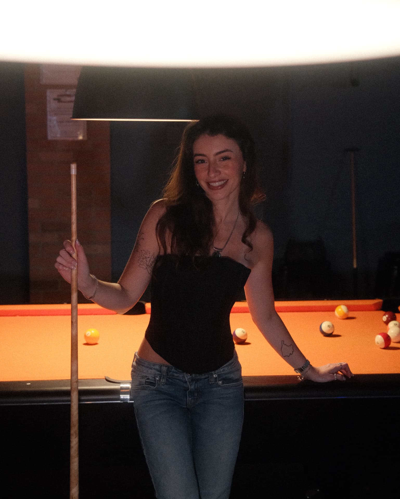 Standing beside the table holding a cue, smiling