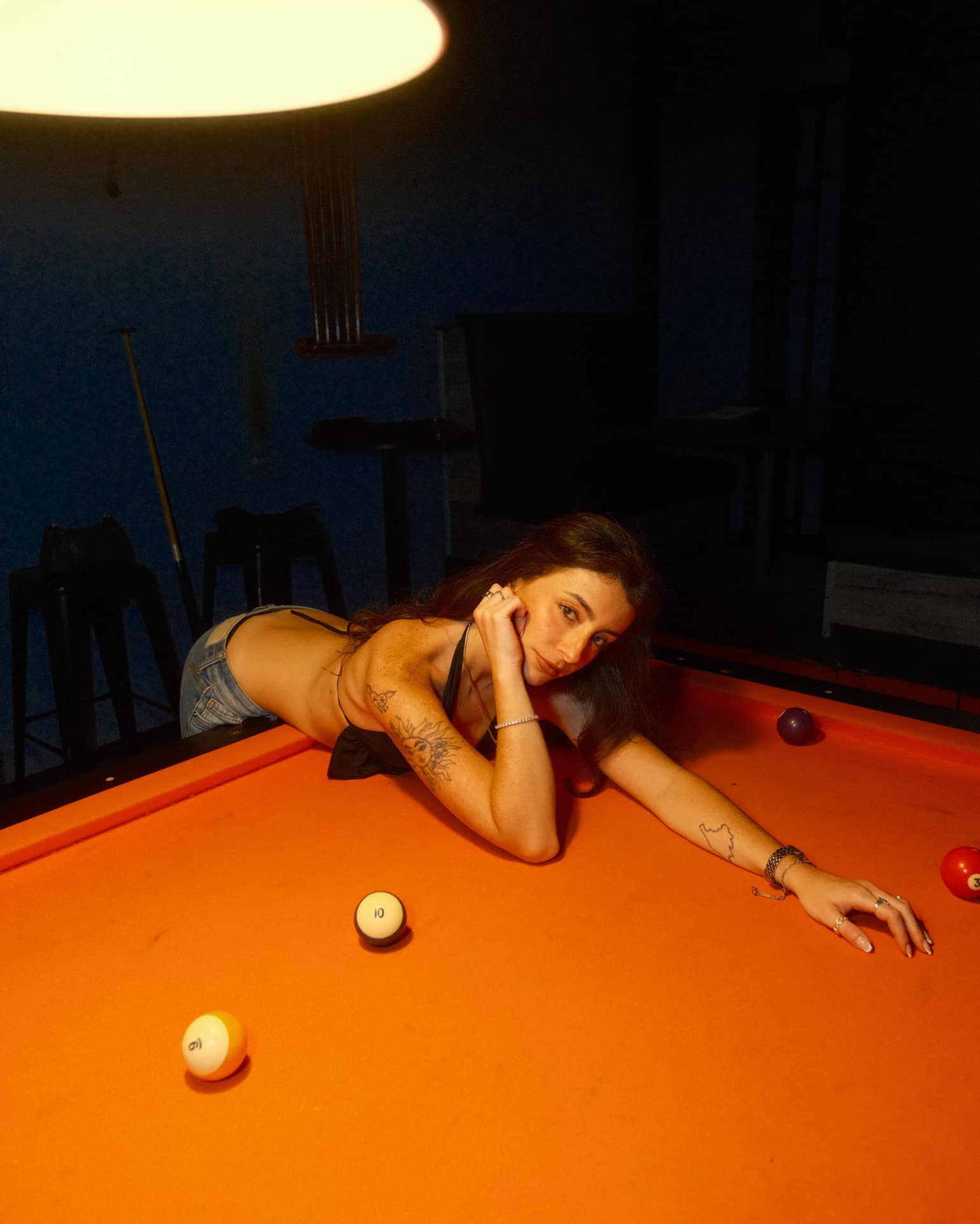 Leaning across an orange pool table under warm overhead light